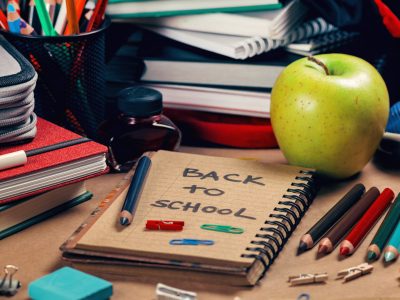 Square composition with school supplies on table. Recycle paper notebook, colored pencils, green apple, books, sharpener, red ink and blue eraser. Back to school concept.
